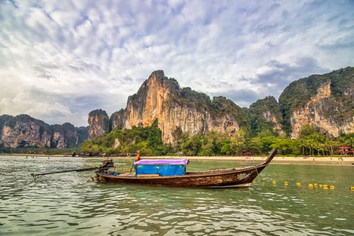 A wooden boat in the sea, trees, and cliffs on the island in Thailand