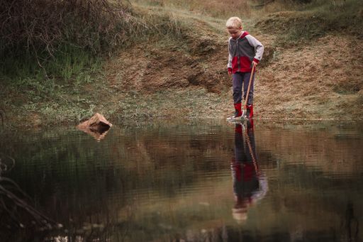 A little boy collecting rubbish from a lake with a net