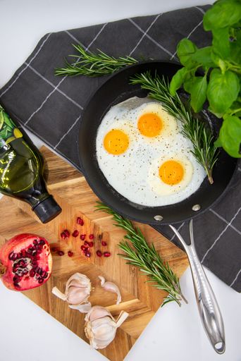 An iron pan with three eggs with herbs and spices, arranged in an aesthetically pleasing arrangement