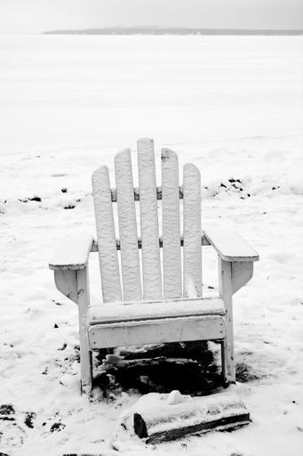 A vertical grayscale shot of a wooden garden chair in a snowy forest