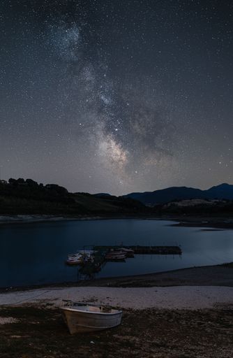 A breathtaking view of starry night sky over a lonely boat on the sandy beach
