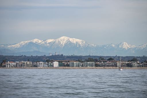 Snow capped mountains form backdrop to Los Angeles skyline (DTLA) and beach from Pacific Ocean post Atmostpheric River Storms.