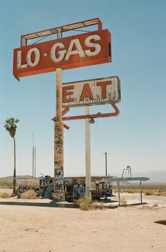 A vertical view of vintage neon road sign boards at a gas station