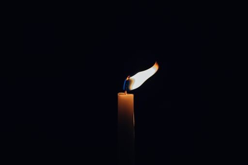 A clsoeup shot of a lit candle with its flame deviated from the wind isolated on black background