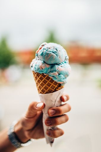 A vertical shot of a cone ice cream with bubble flavour in a girl's hand on abstract background