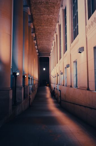 A vertical shot of a narrow hallway alongside the columns with an illuminated lamp in the end