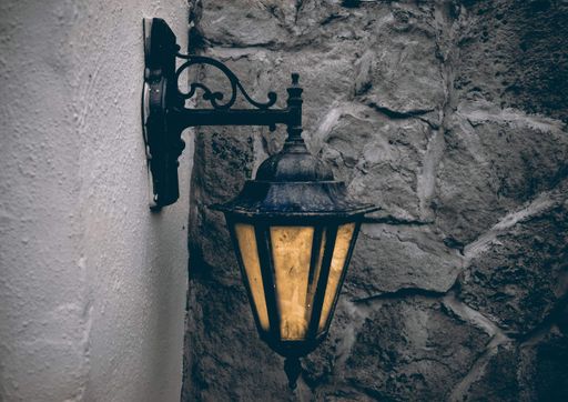 A closeup shot of an old-fashioned lantern on a white building against a stone wall