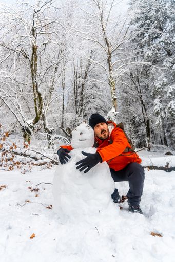 A funny man hiker joking with a snowman in the snowy forest of the Artikutza natural park in San Sebastian, Basque Country, Spain