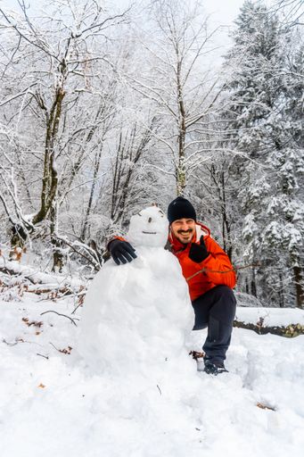 A funny man hiker joking with a snowman in the snowy forest of the Artikutza natural park in San Sebastian, Basque Country, Spain
