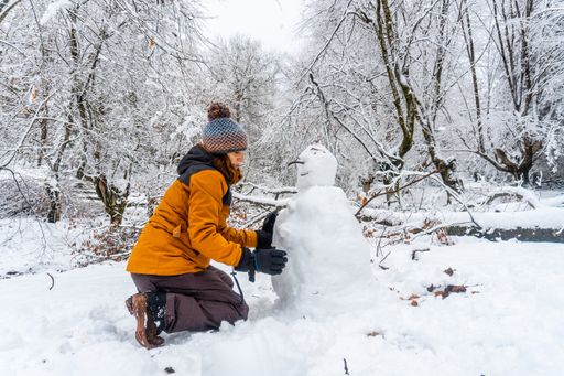 A young Caucasian woman making a snowman in the snowy forest of the Artikutza natural park in San Sebastian, Basque Country, Spain
