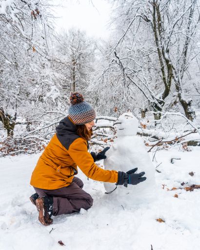 A young Caucasian woman making a snowman in the snowy forest of the Artikutza natural park in San Sebastian, Basque Country, Spain