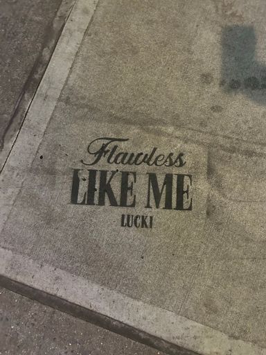 A closeup of FLAWLESS LIKE ME graffiti on a sidewalk ground
