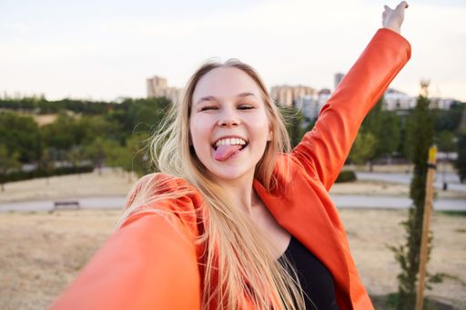 A young female standing with arms outstretched, taking a selfie with a humorous expression on her face