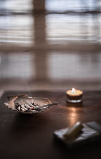 A vertical shot of an ashtray full of burnt cigarettes and a burning candle in the blurred background
