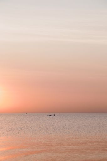 A vertical shot of people in a boat in the calm sea during a scenic sunset