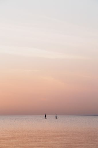 A vertical shot of people surfing in the calm sea on a cloudy day