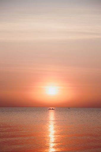 A vertical shot of people in a boat in the calm sea during scenic sunset