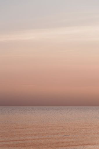 A vertical shot of the calm sea and the cloudy sky during sunset