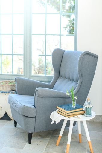 A vertical shot of a comfortable blue armchair near a small table with books in a corner of the house