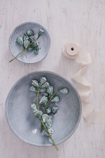 A vertical top view of decorative dried flowers in small ceramic cups and a bobbin of white ribbon
