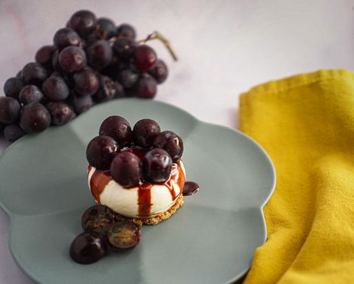 A close-up shot of grape cheesecake with sauce in gray plate