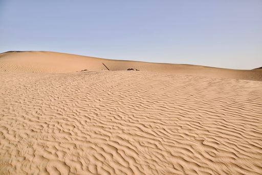 A scenic view of desert against sky under the clear blue sky with the sun shining bright