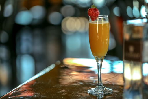 A closeup of an orange drink with a strawberry on the table with a blurry background