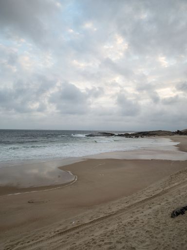 A vertical shot of a sandy beach and wavy sea under cloudy sky