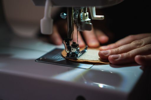 A close-up of a person sewing using a sewing machine, illuminated by a lamp