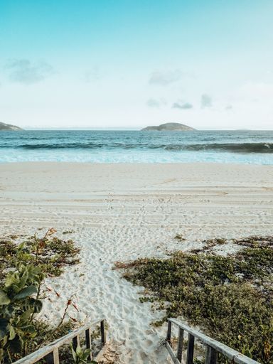 A vertical shot of a sandy beach and wavy sea under blue sky