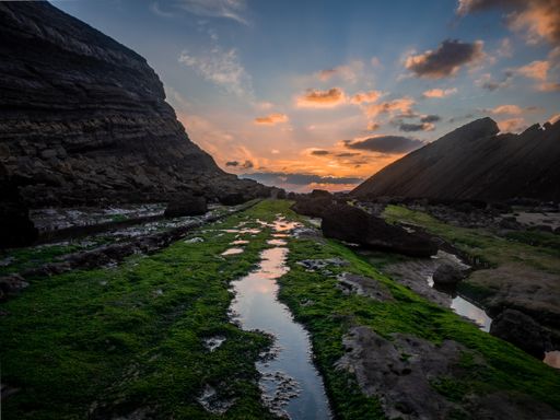 The water paths and rocks covered with green moss in Madero beach in Liencres, Cantabria at sunset