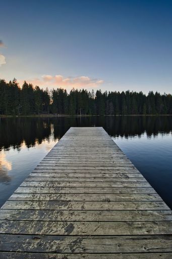 An idyllic scene of a wooden dock extending out onto a serene lake at sunset