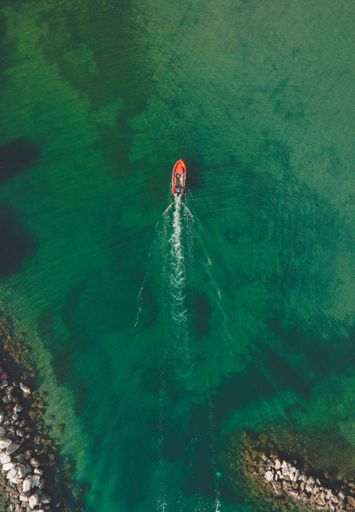 A vertical top view of a red boat sailing on green water