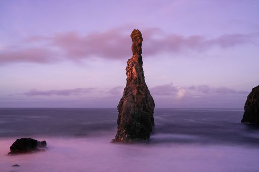 A scenic view of the rock surrounded by sea on a foggy day during sunset