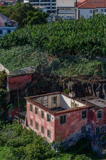 An aerial shot of a pink abandoned building surrounded by green grass and trees