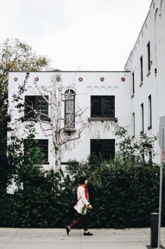 A vertical shot of an Asian female in a long-sleeved shirt walking near the white buildings