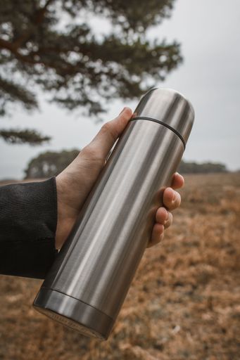 A vertical closeup shot of a person holding a stainless steel coffee thermos