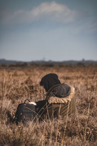 A vertical back view of a young male with backpack sitting in a field on a sunny day