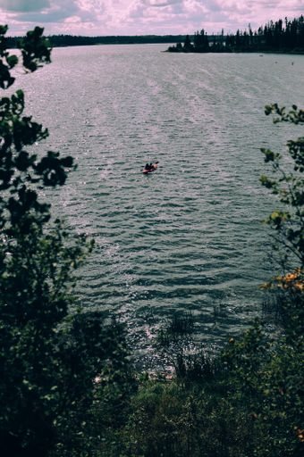 A vertical high angle shot of a person sailing in a boat in the calm lake under the cloudy sky
