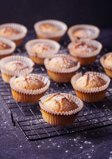A vertical shot of baked lemon muffins with powder put on a metallic tray isolated on dark background