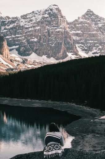 A vertical high angle shot of a female sitting near the Moraine Lake and admiring the snowy mountains