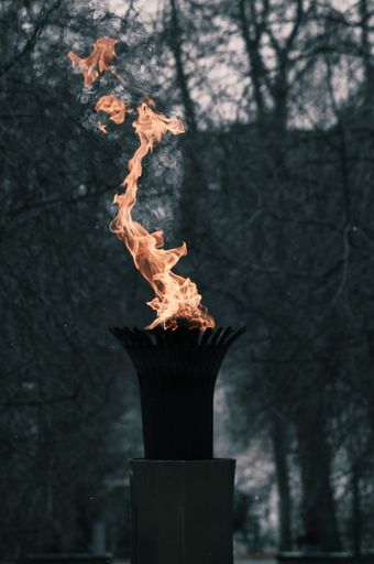 A vertical closeup shot of the flame getting out of a flambeau with trees in the background