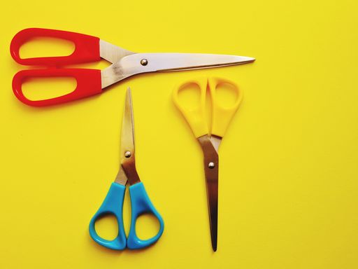 An overhead shot of three pairs of colored scissors on a yellow background