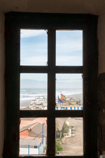 A scenic view of a beach through a window, with a few boats parked on the beach