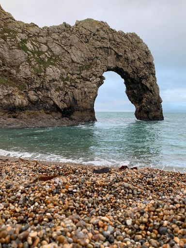 A vertical shot of Durdle Door Beach with colorful rocks and big, gray cliffs on the coast