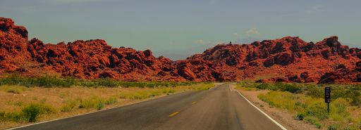 A panoramic view of an asphalt highway surrounded by orange-shaded sand covered with grass and mountains