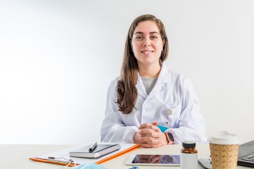 A young professional female doctor sitting in her consulting room smiling in front of the camera