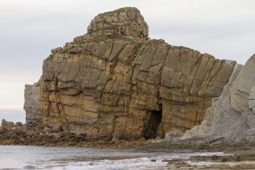 A closeup shot of a cliffy seashore near a wavy sea under a cloudy sky