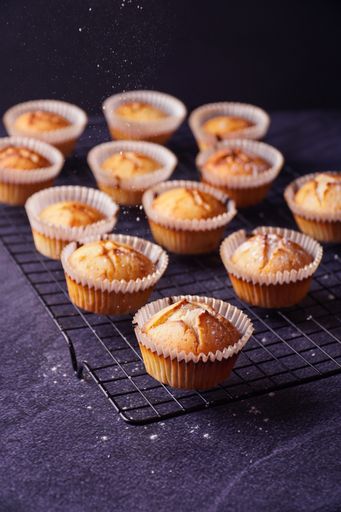 A vertical shot of baked lemon muffins with powder put on a metallic tray isolated on dark background