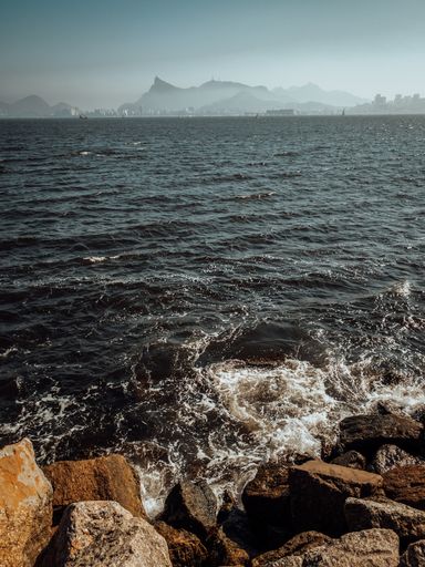 A vertical shot of a rocky beach and wavy sea under blue sky